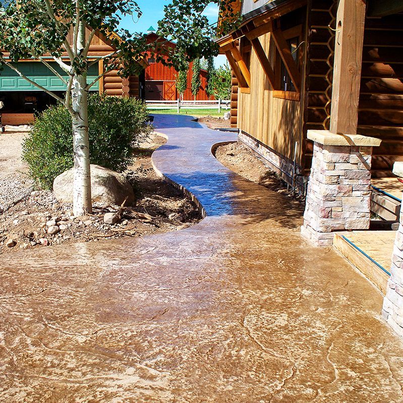 Wet concrete walkway between log cabins and landscaped rocks in a sunny outdoor area