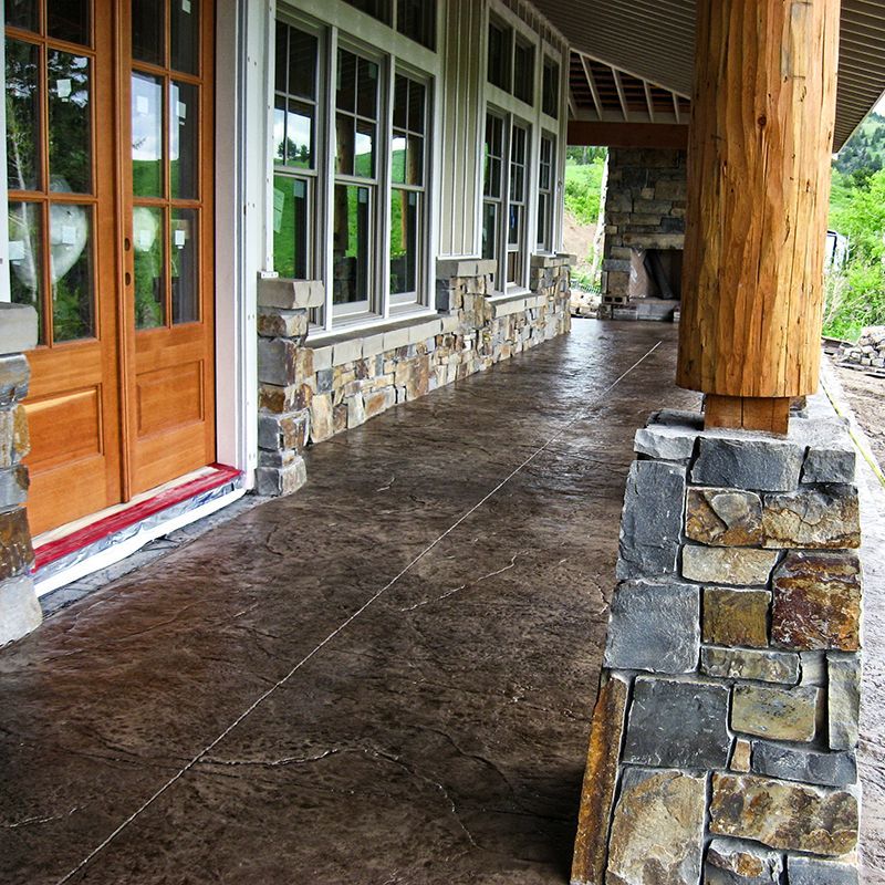 Covered stone-and-wood porch with windows, wooden door, and wet concrete floor.
