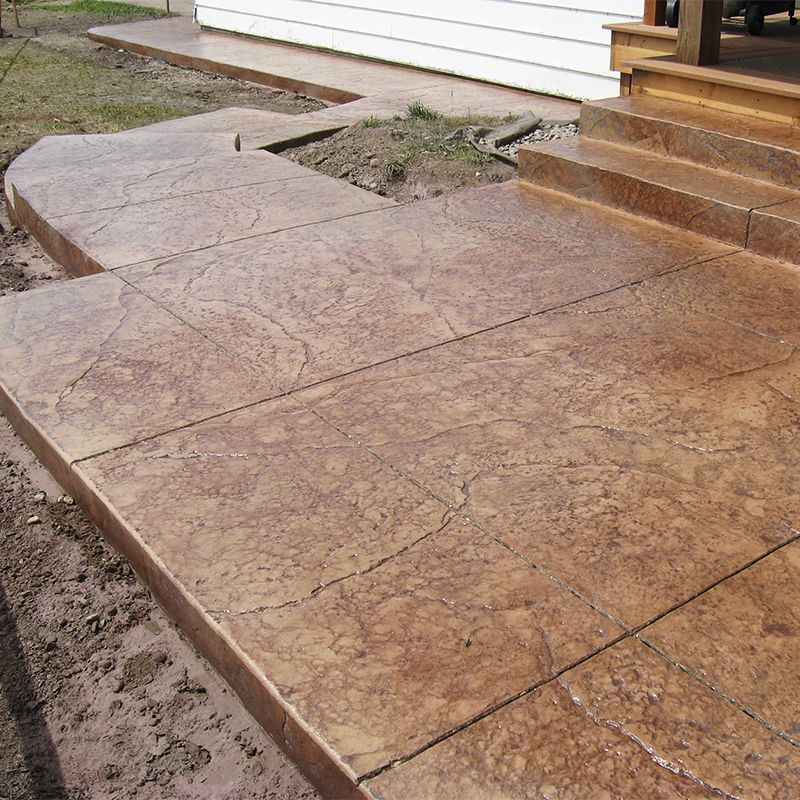 Stamped concrete walkway and steps beside a house, with a curved landing and dirt edging