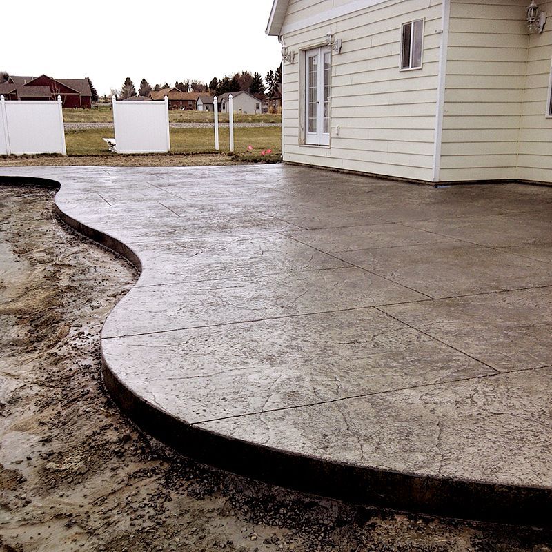 Curved concrete patio beside a white house, with muddy ground and a yard in the background
