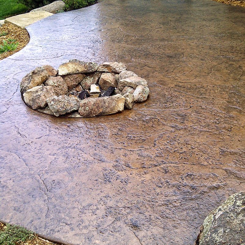 Stone fire pit set in a wet stamped concrete patio in a yard.