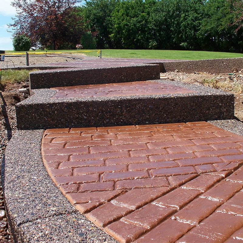 Brick path with two low steps leading to a grassy park under bright daylight