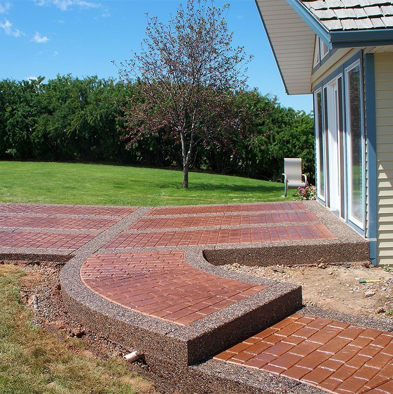 Curved brick patio steps beside a house with sliding doors, overlooking a green lawn and trees.