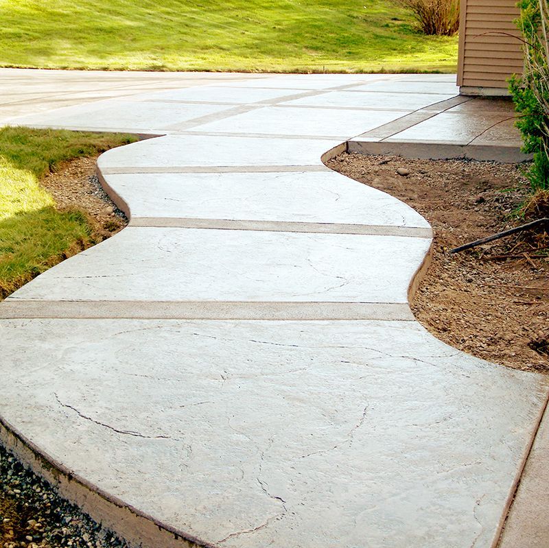 Curved concrete sidewalk beside a grassy yard and wooden building exterior