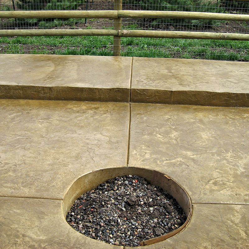 Shallow round pit filled with rocks in a concrete platform, with bamboo railings in the background
