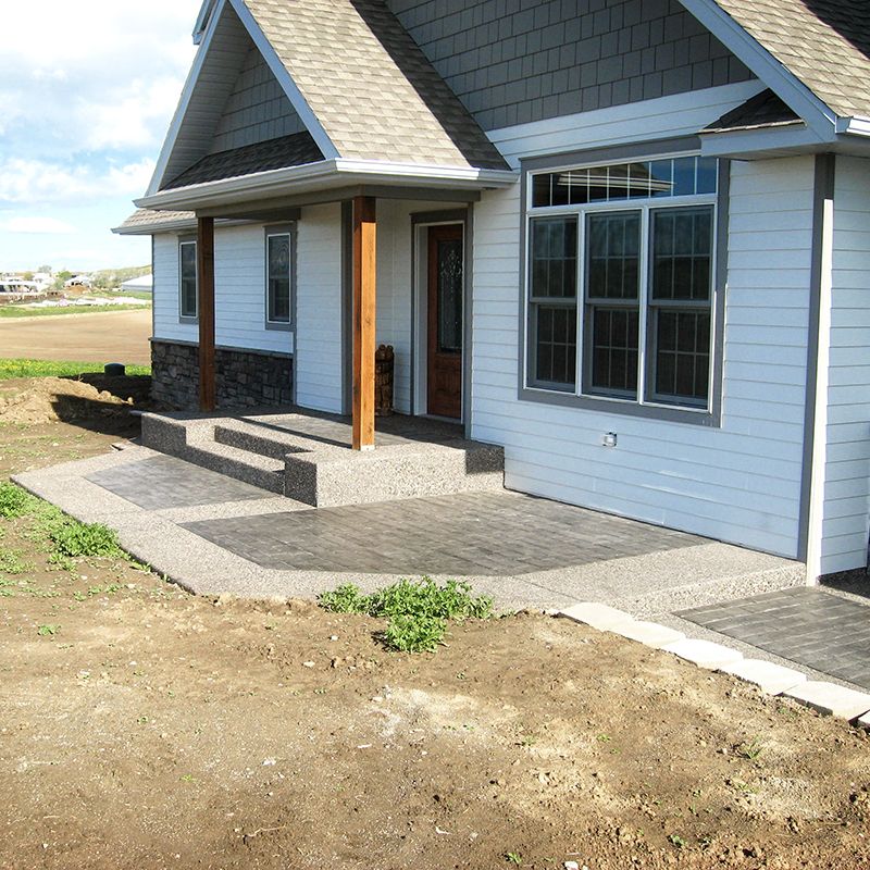 Front porch of a gray house with steps, wooden posts, and a large window beside a dirt yard.