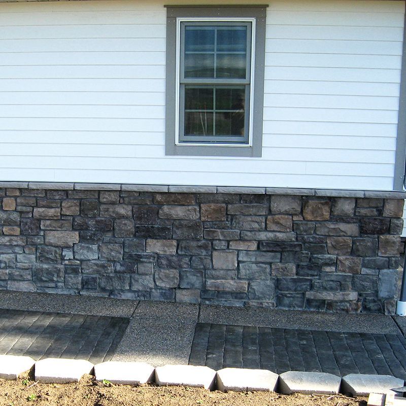 White house wall with a small window above a stone foundation and paved walkway in front