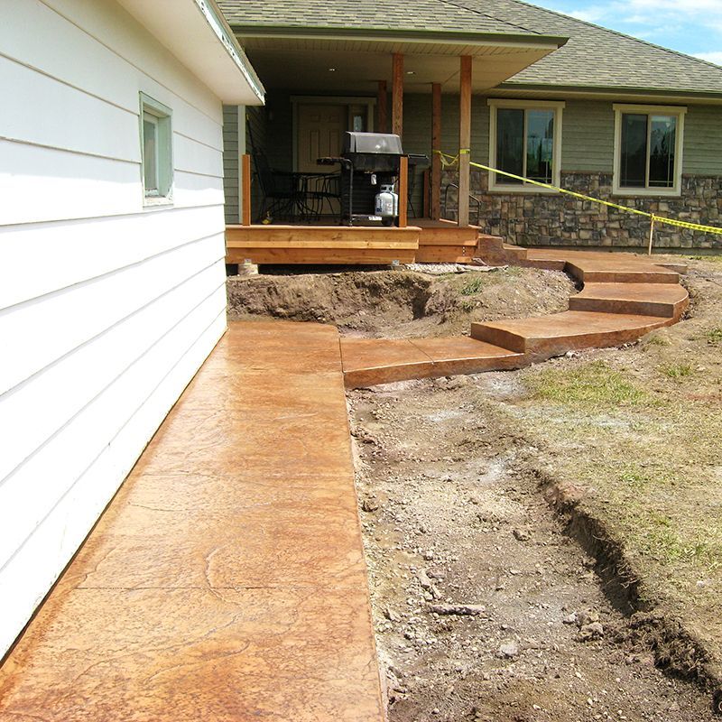 Front walkway under construction beside a house, with a concrete path and steps leading to a porch.