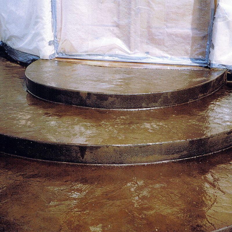 Two-tiered round stage platform with dark wooden edges on a brown floor, against a translucent backdrop.