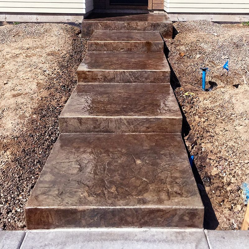 Concrete walkway steps leading to a house entrance, bordered by gravel and blue utility markers