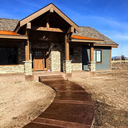 Front entrance of a rustic house with stone pillars and a curved brown walkway under a blue sky
