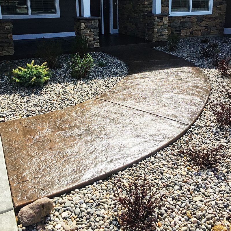 Curved stamped concrete walkway bordered by decorative rocks leading to a house entrance