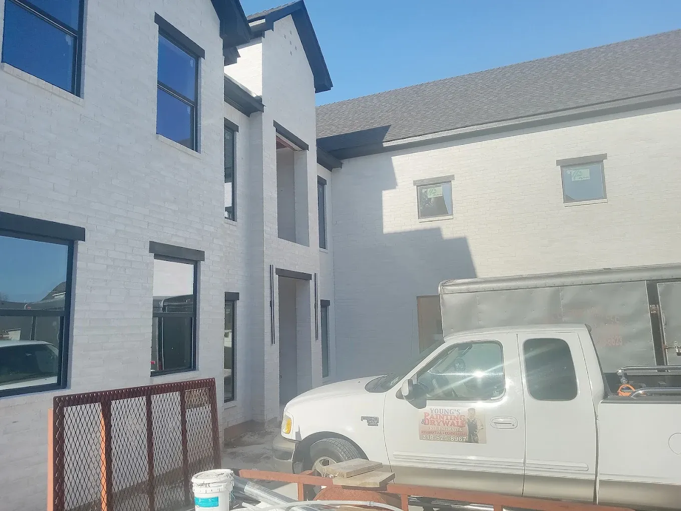 Two-story white building under construction with a white pickup truck and a sunny sky.