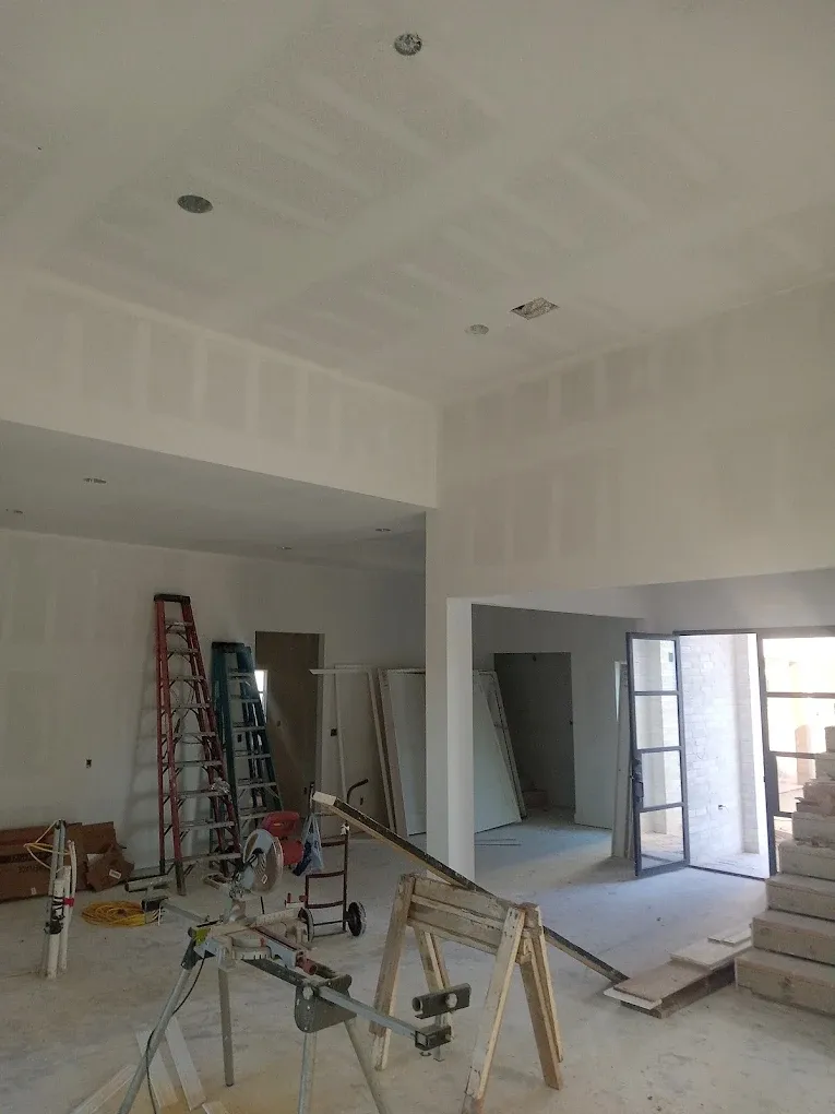 Interior construction site with drywall on walls and ceiling, ladders, tools, and unfinished flooring.