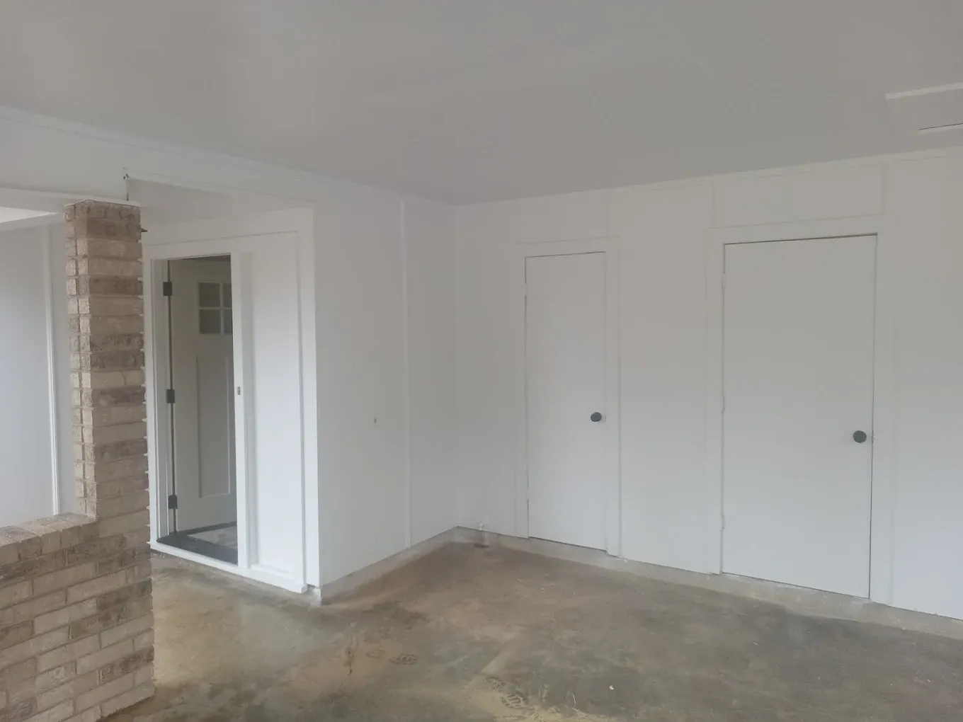White-walled room with three doors, brick pillar, and a doorway to another room.