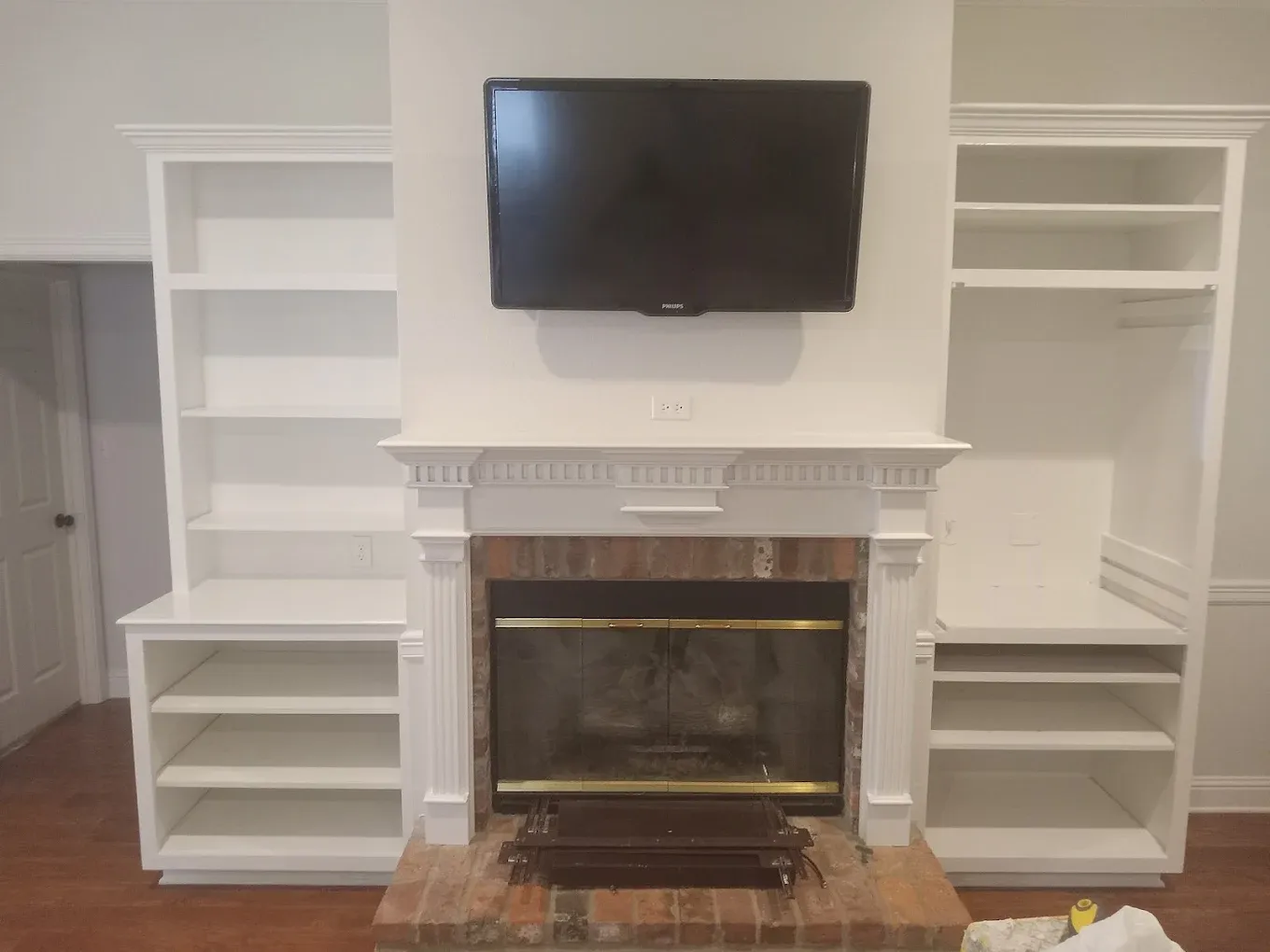 Built-in white bookshelves flank a brick fireplace with a mounted TV above the mantel.