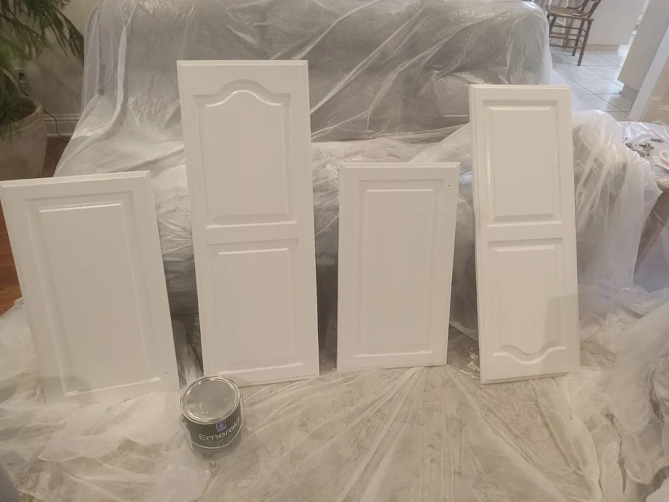 Four white cabinet doors leaning against a covered sofa, prepared for painting.