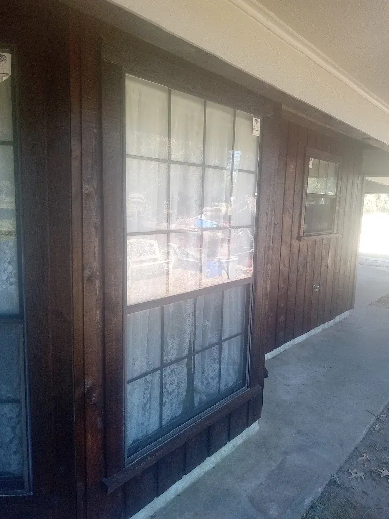 Dark brown wooden building with a large window and a small window, with a concrete pathway.