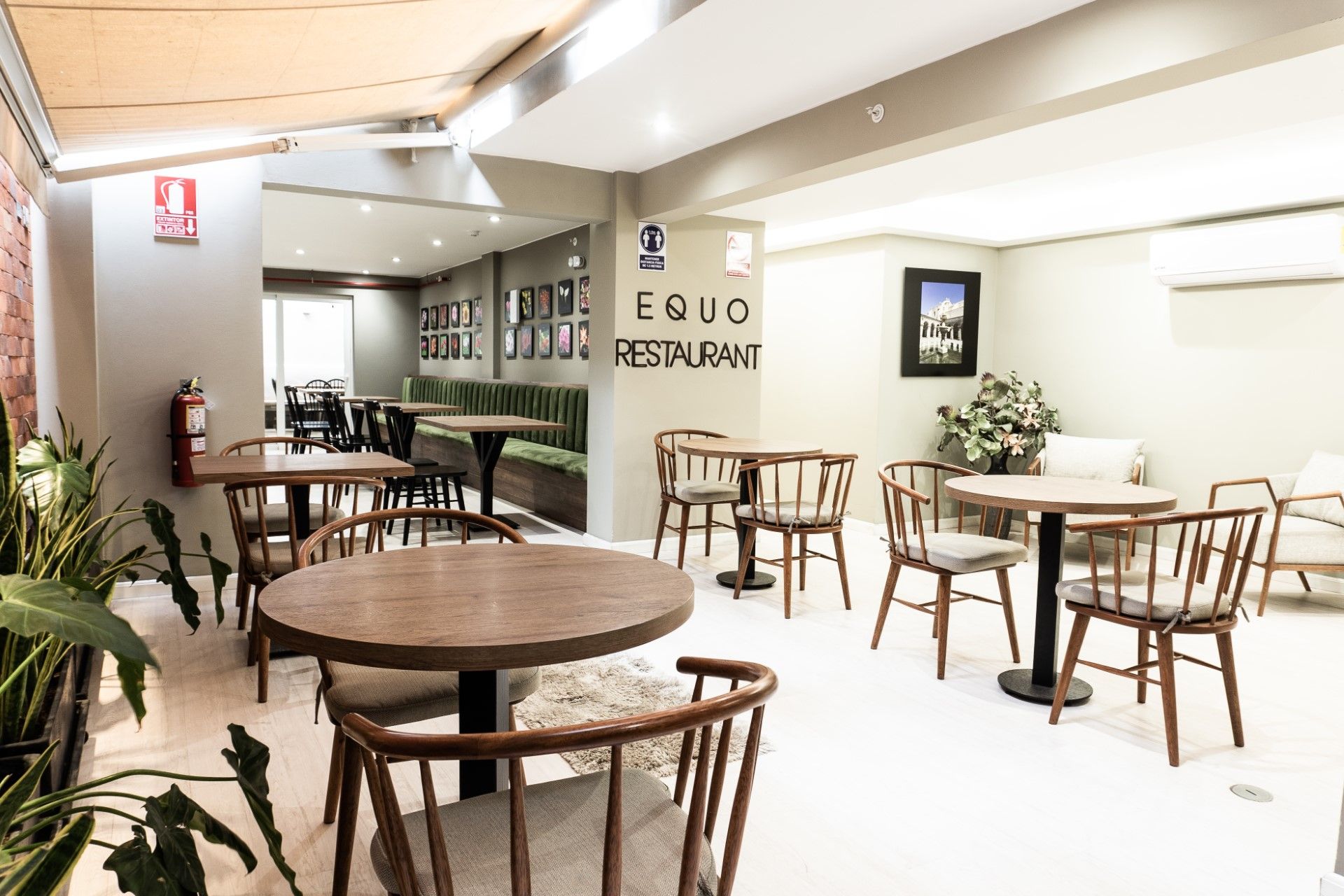 Interior de restaurante con mesas y sillas de madera y macetas con plantas. Letrero 