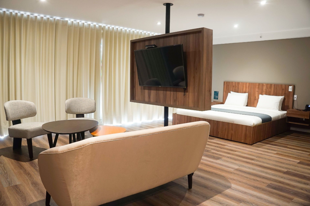 Habitación de hotel con TV, escritorio, mininevera y cama. Combinación de colores marrón y gris.
