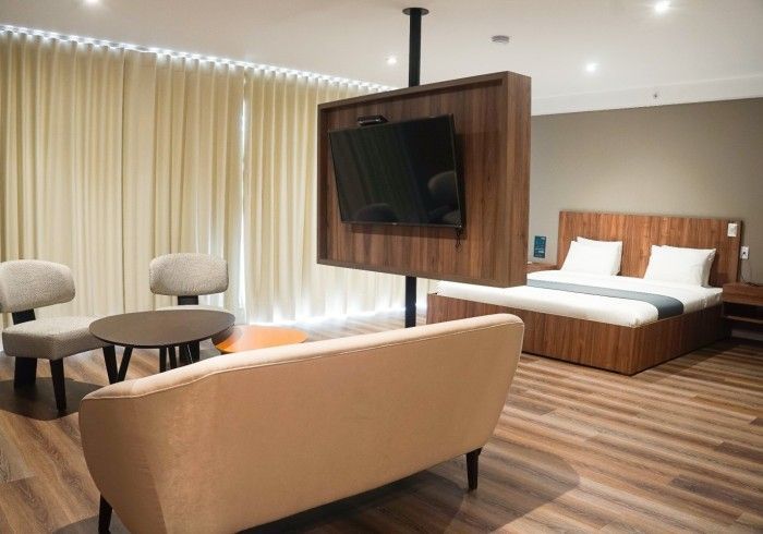Habitación de hotel con una cama, zona de estar y un televisor montado en un poste vertical.