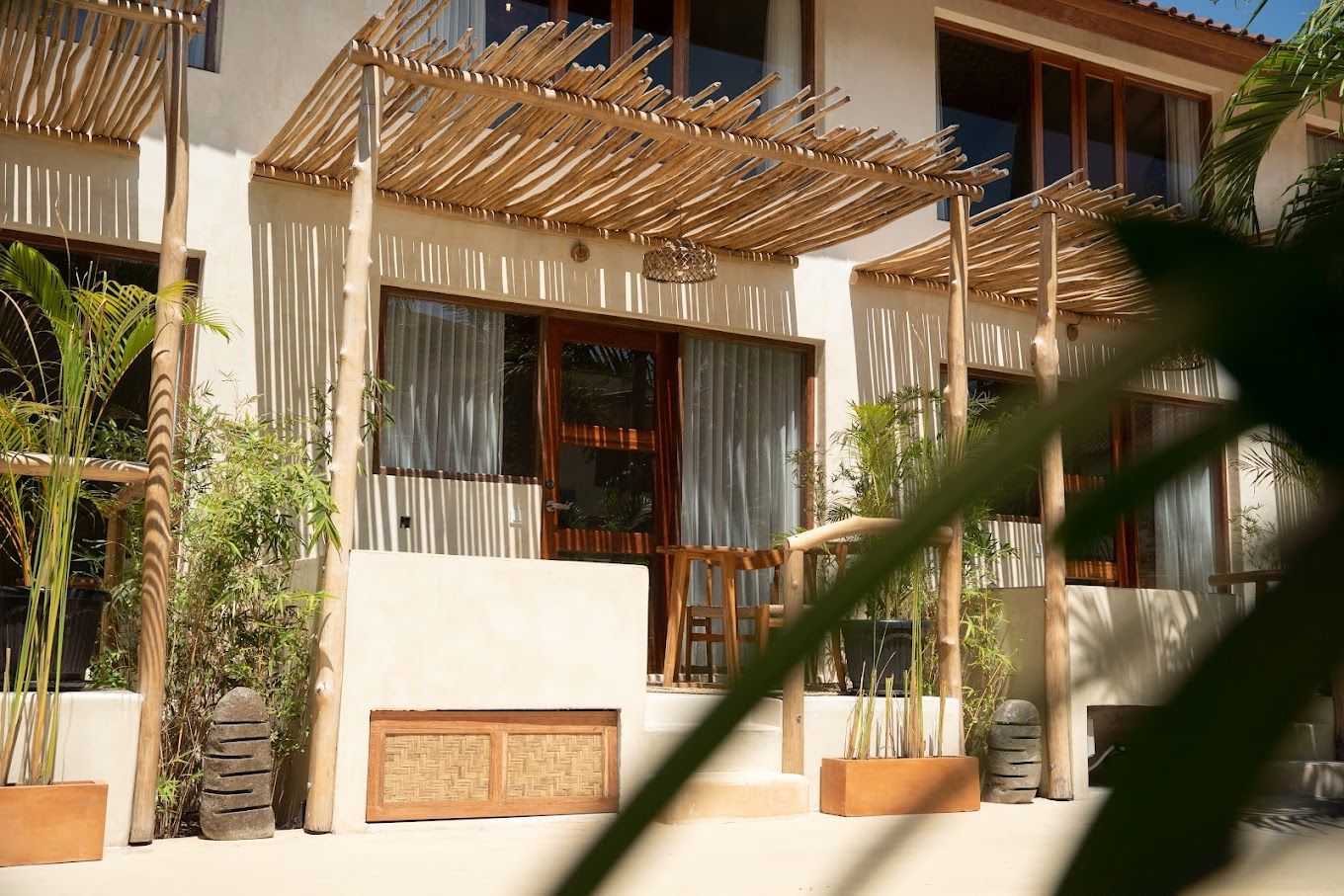 White building with bamboo accents, plants, and open doorway with light-colored curtains.
