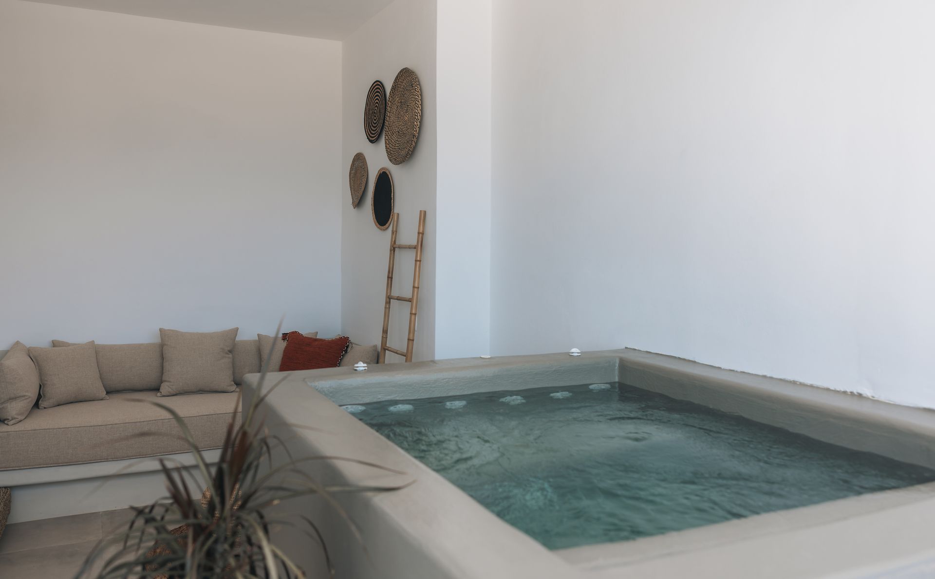 Outdoor jacuzzi and lounge area with white walls, beige cushions, and decorative wall baskets.