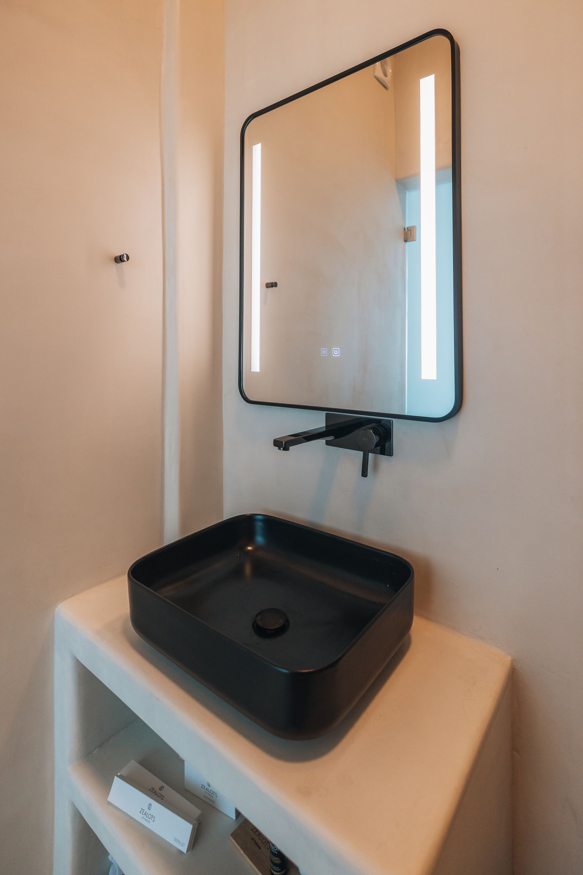 Black square sink on white pedestal with a black-framed mirror with lights. Modern bathroom.