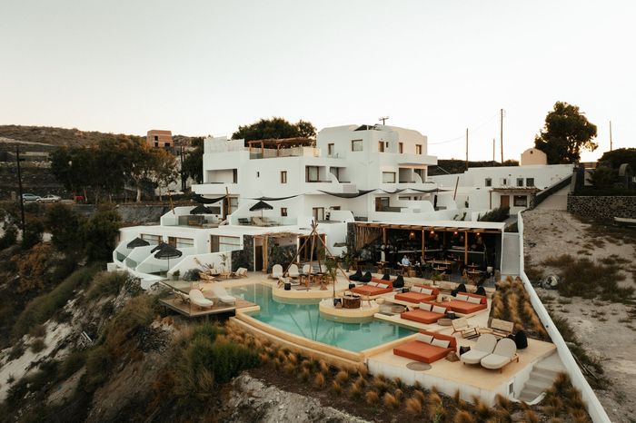 White hotel with a pool, lounge chairs, and a bar on a cliff overlooking the ocean.