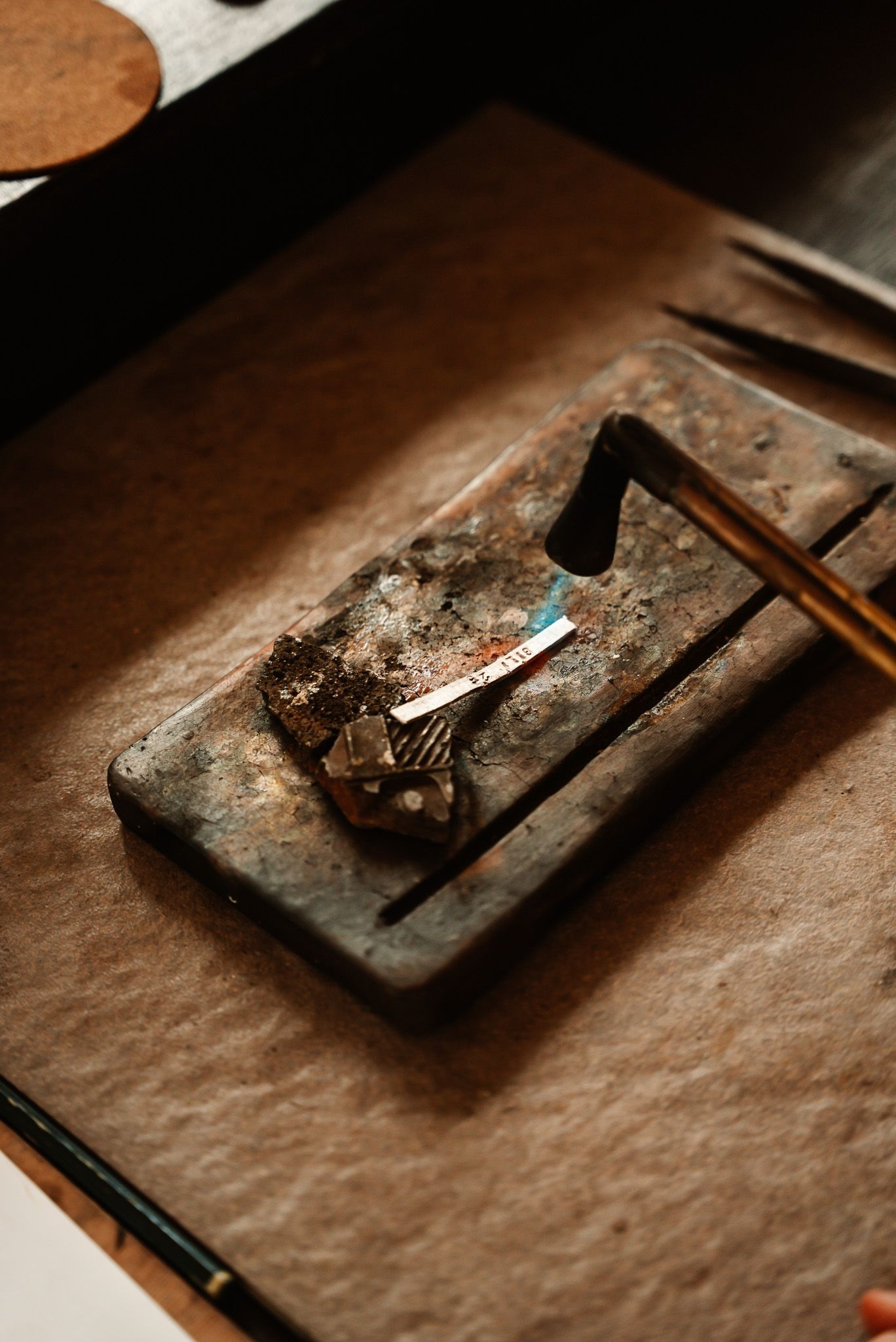 Jeweler using a torch to solder a small silver piece on a heat-resistant surface.