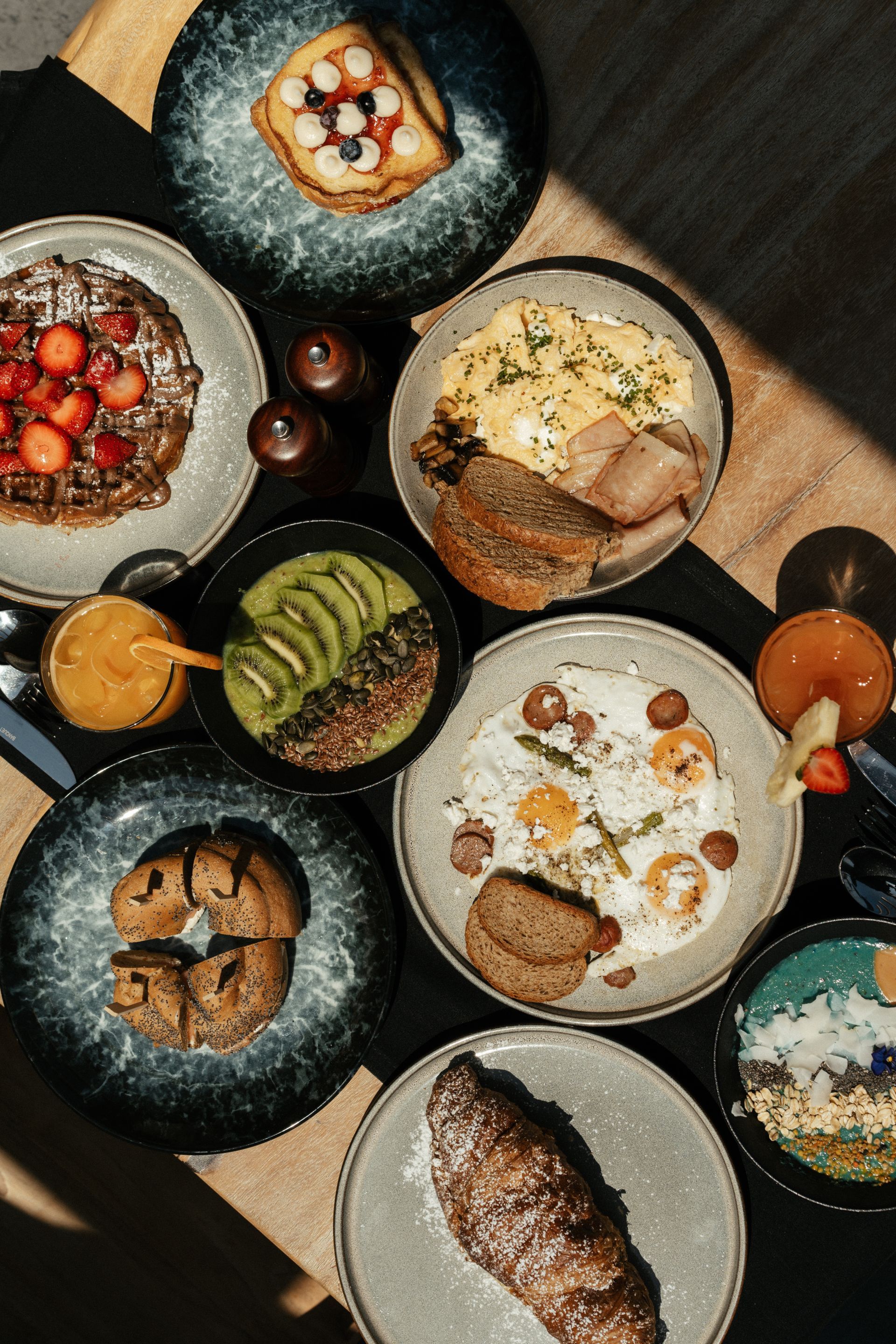 Assortment of breakfast dishes on plates, including waffles, eggs, fruit, and pastries.