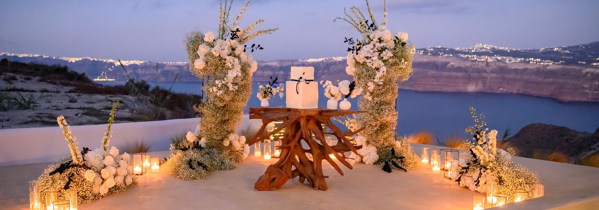 Wedding altar with floral arch overlooking a caldera at dusk.