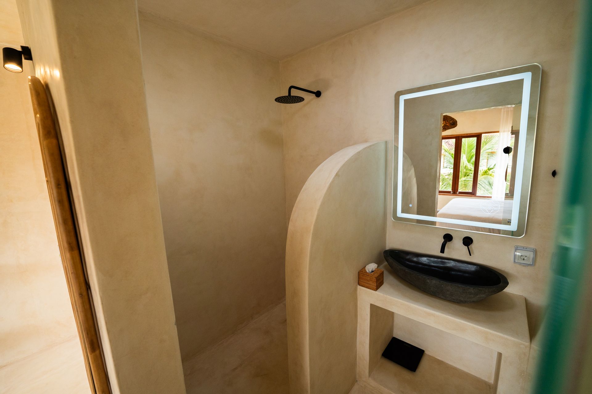 Neutral-toned bathroom with walk-in shower, black sink, and illuminated mirror. Doorway on left.