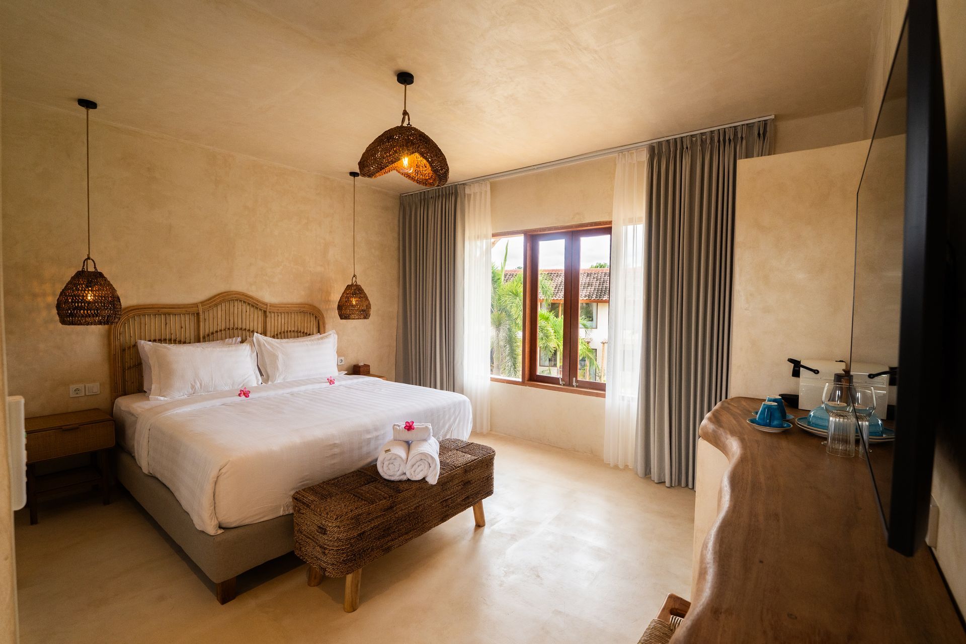 Bedroom with king bed, neutral tones, wicker accents, window with curtains, and a large TV.