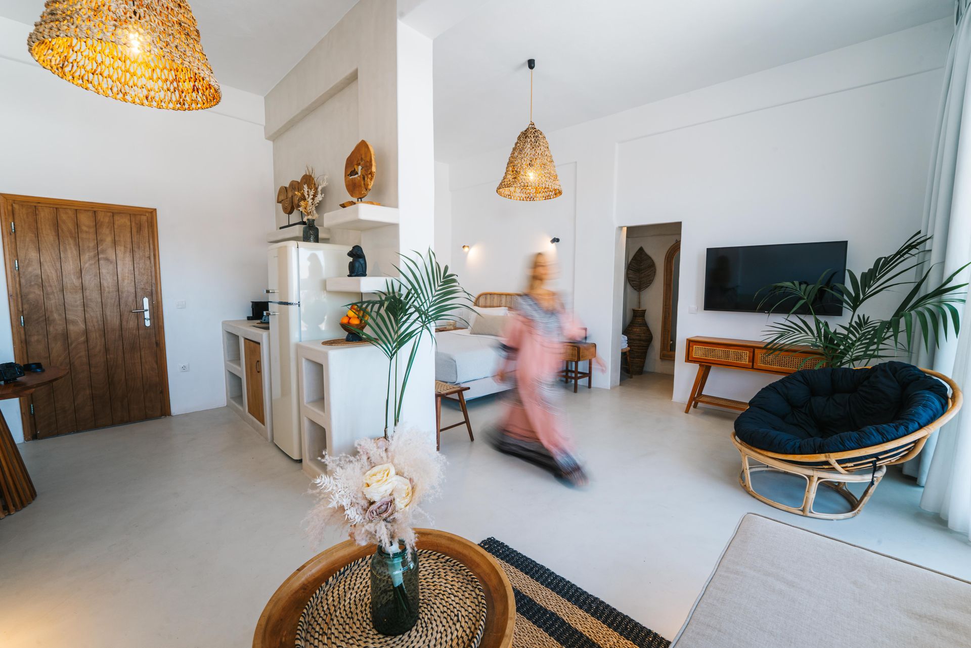 Bright, airy room with a blurred figure walking through. White walls, natural wood and woven accents.