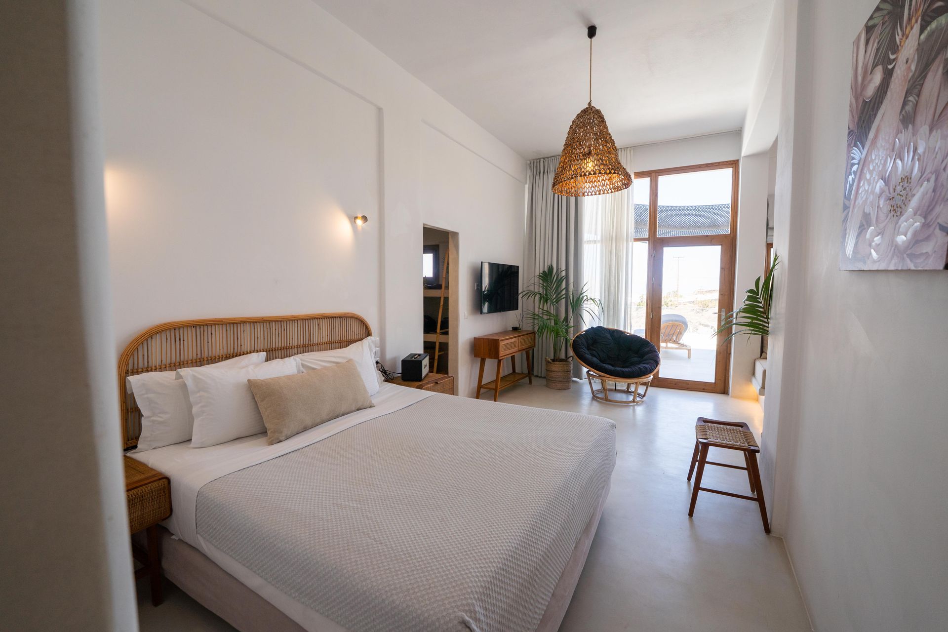 Bedroom with white walls, bed, seating area, door to outdoor space, and woven lampshade.