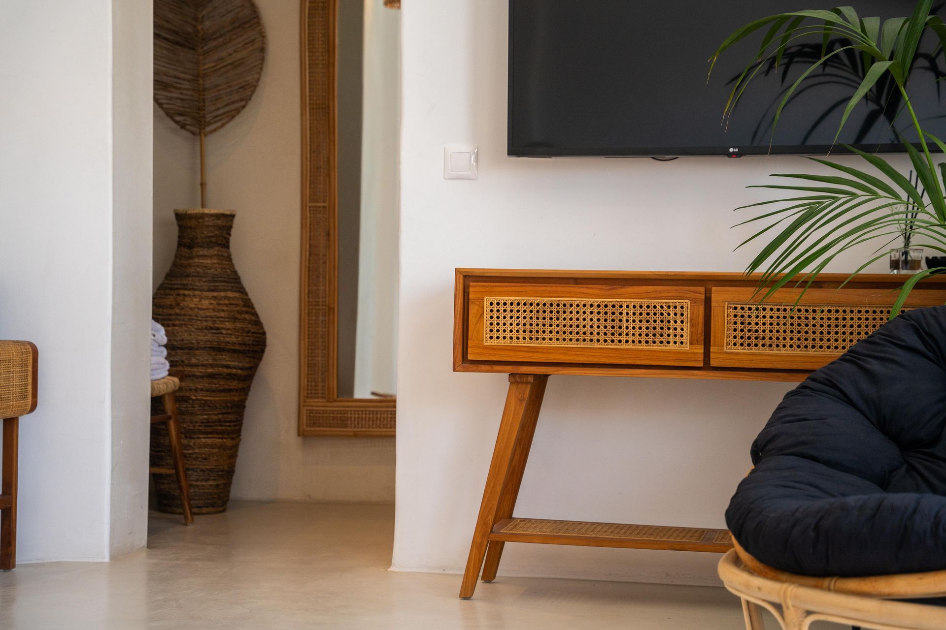 Wooden console table under a TV, with a wicker front, and a black chair.
