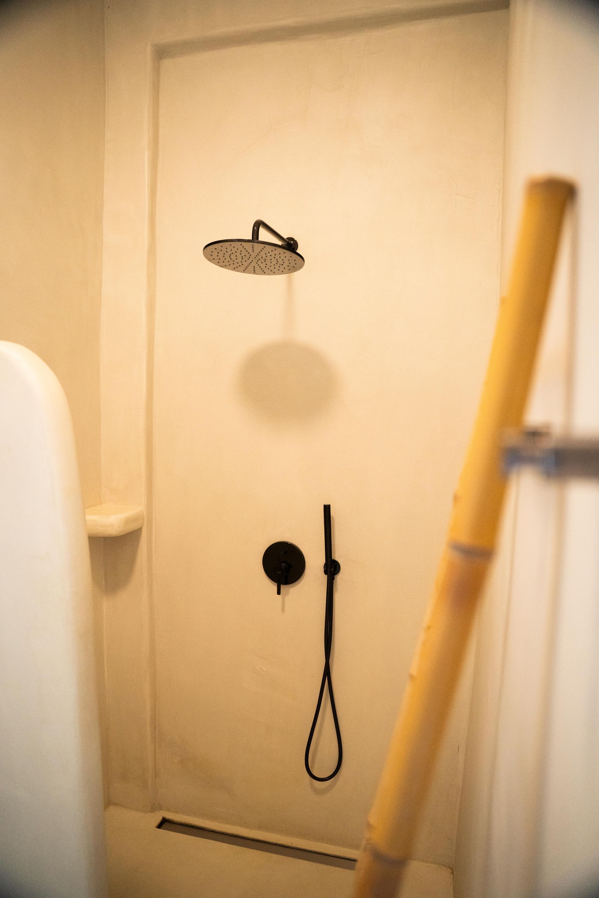 Shower stall with a black showerhead and faucet. A yellow bamboo pole stands in the foreground.