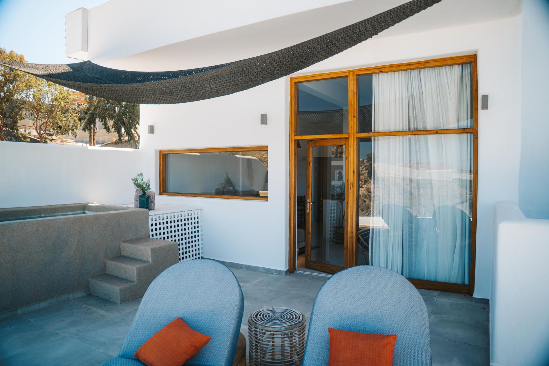 Patio with two chairs, shaded by a canopy, near a door and small pool.