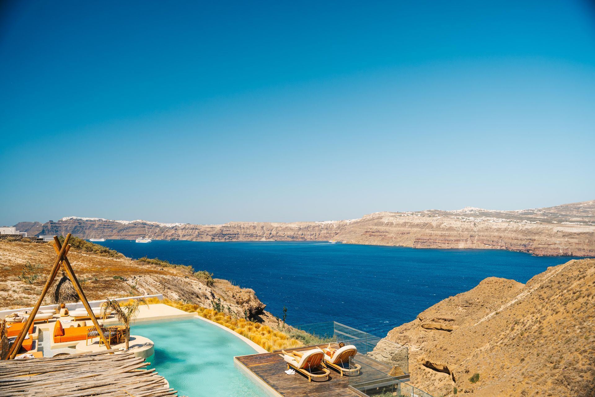 Pool overlooking the Aegean Sea in Santorini, Greece. Blue water and sky; rocky terrain.