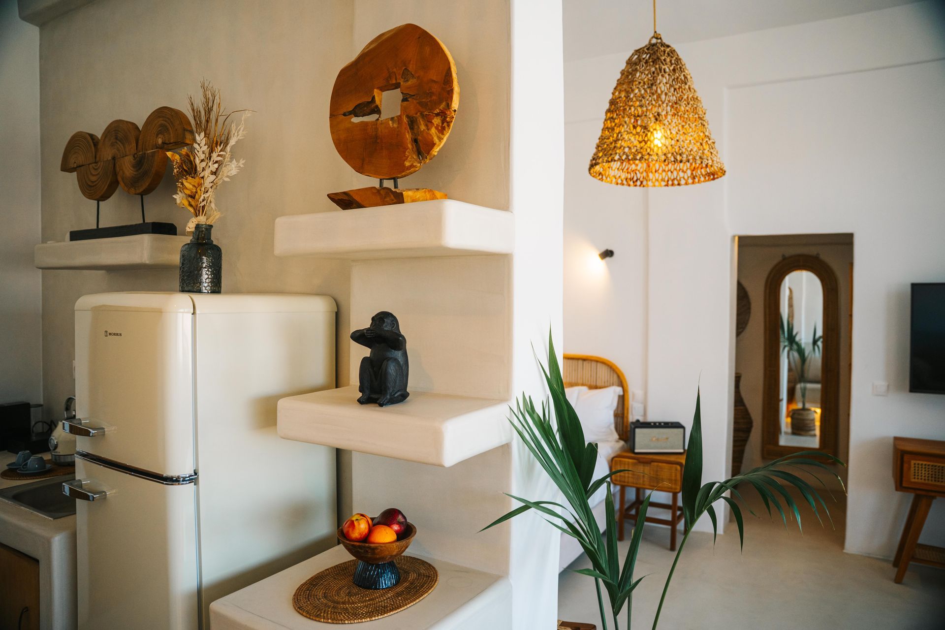 White room interior with shelves holding decor, a cream refrigerator, and woven pendant light.