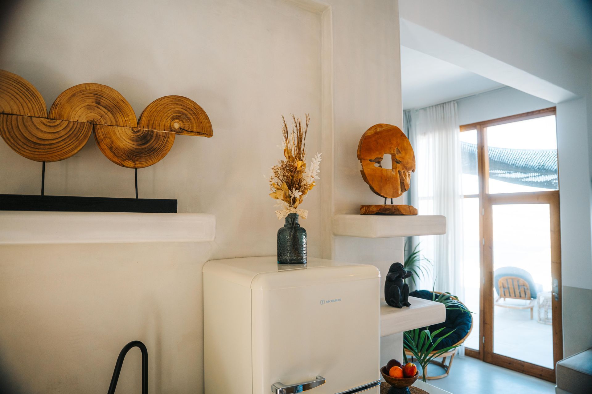 Bright white room with decorative wooden sculptures, a vase of dried flowers, and a retro refrigerator.