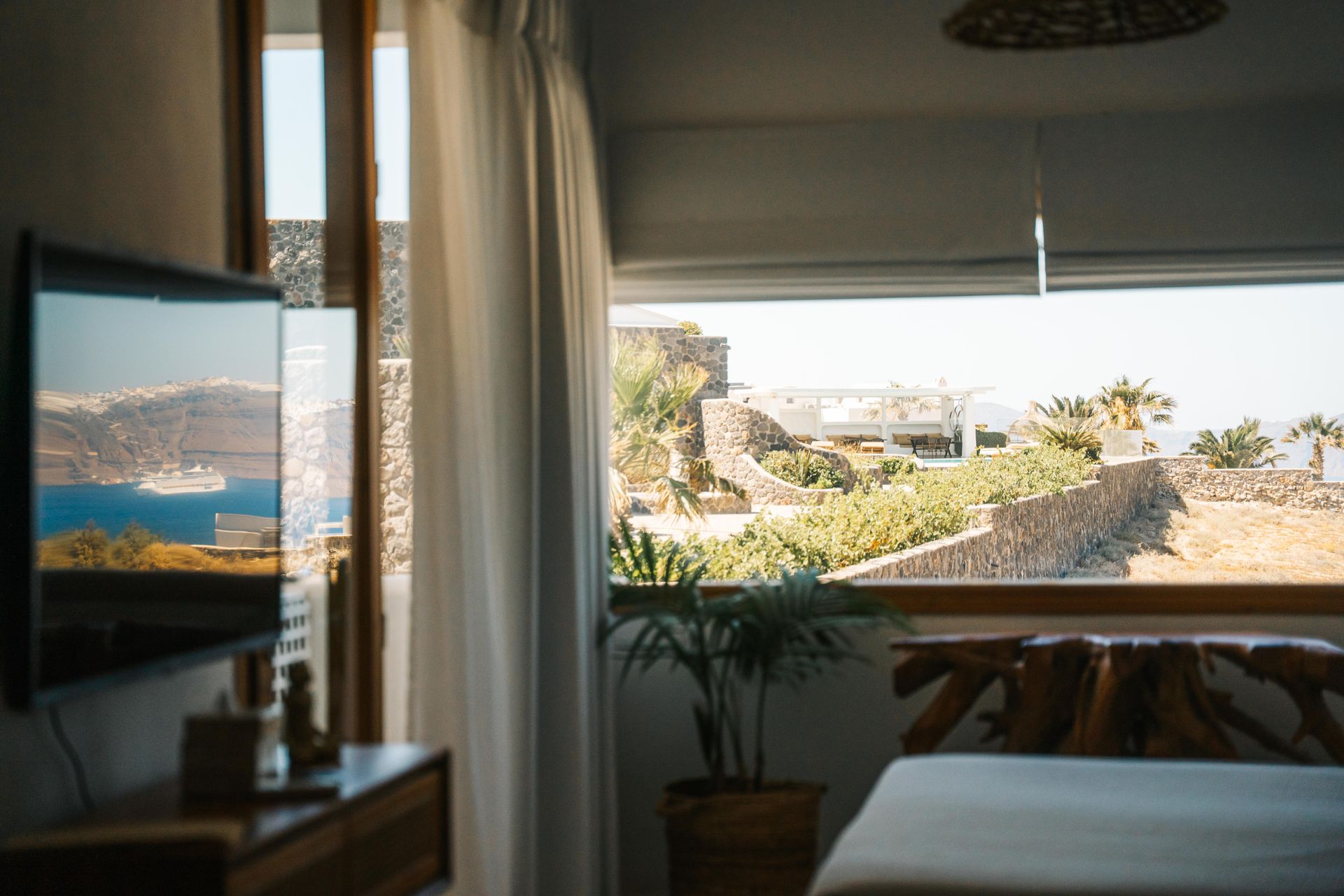 Bedroom with a view of the sea and rocky terrain, a TV on the wall, a bed, and a window.