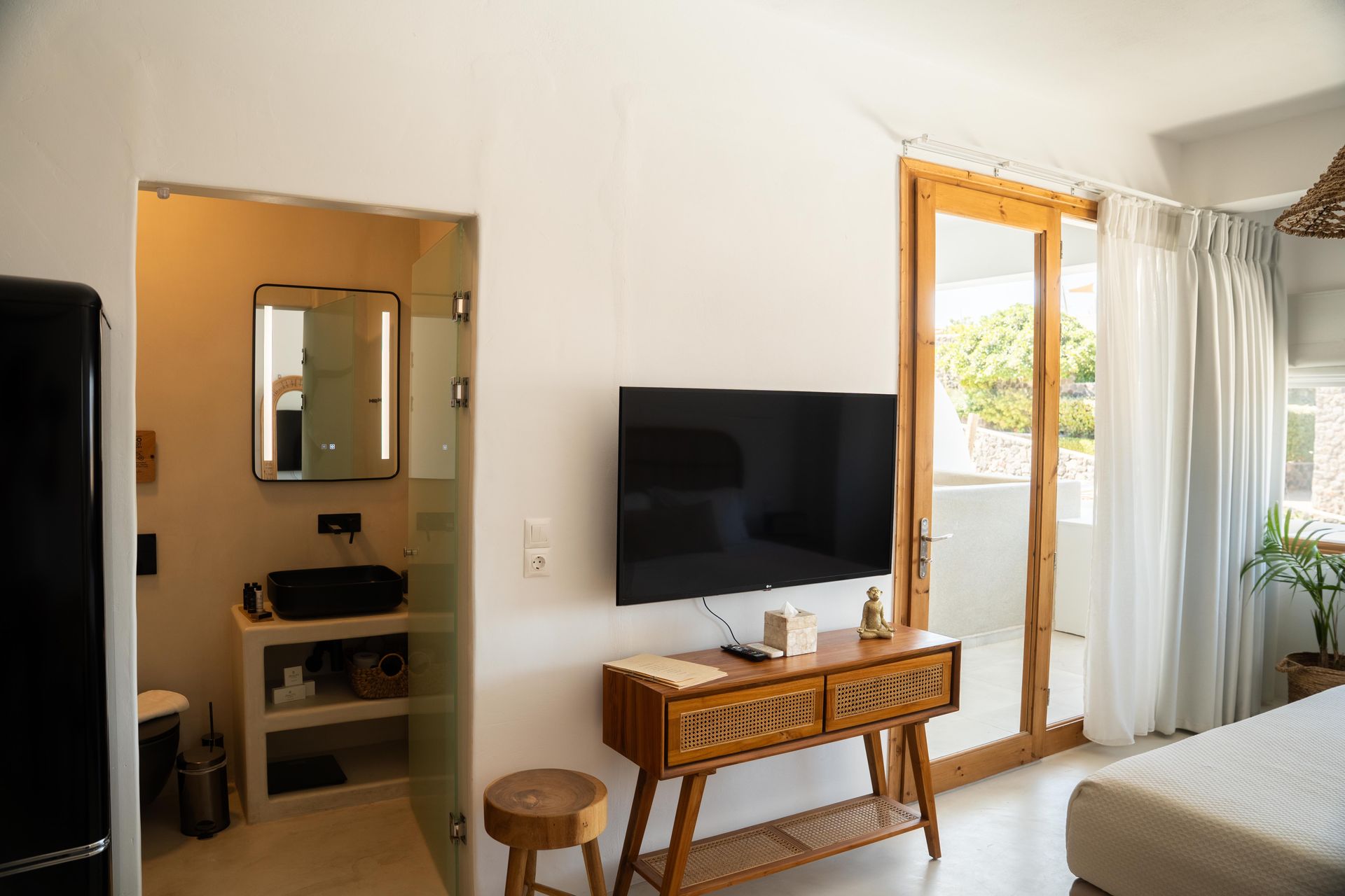 Bedroom with a TV, bathroom, and balcony with white walls and wooden accents.