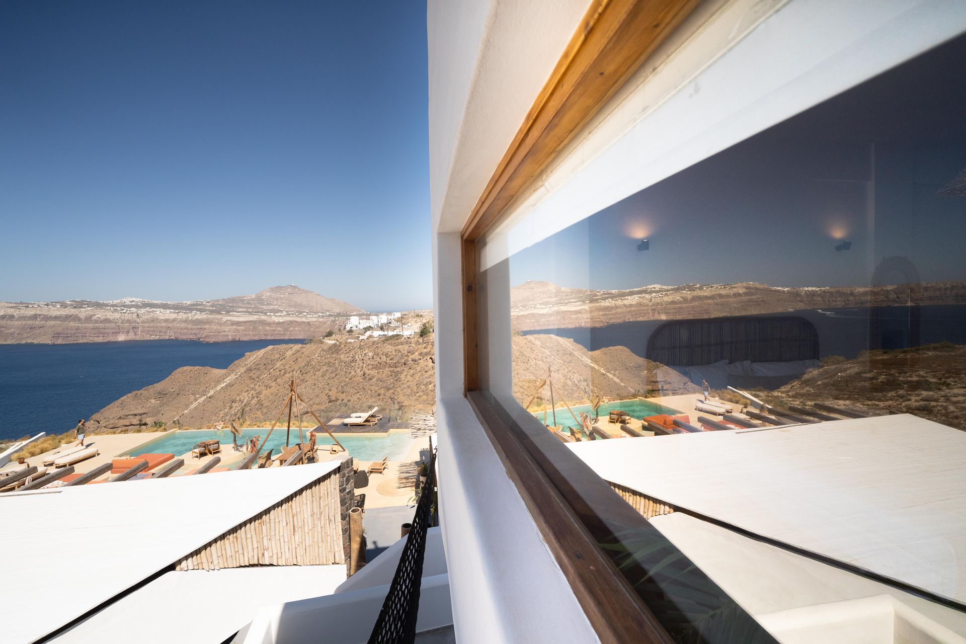 View from a window overlooking the sea, white buildings, pools, and a clear blue sky.