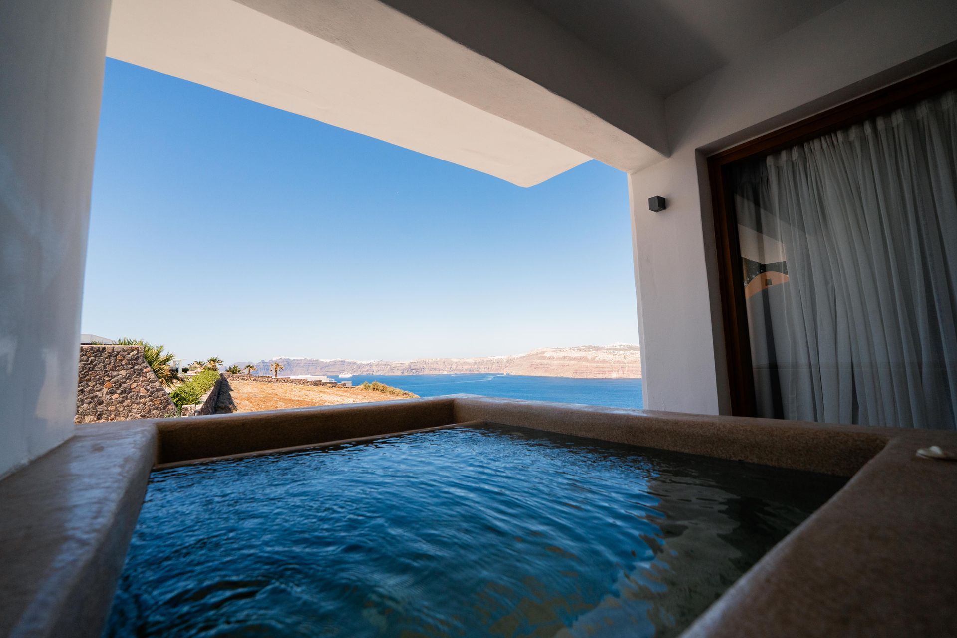 Hot tub overlooking the ocean, framed by white walls and a bright blue sky.