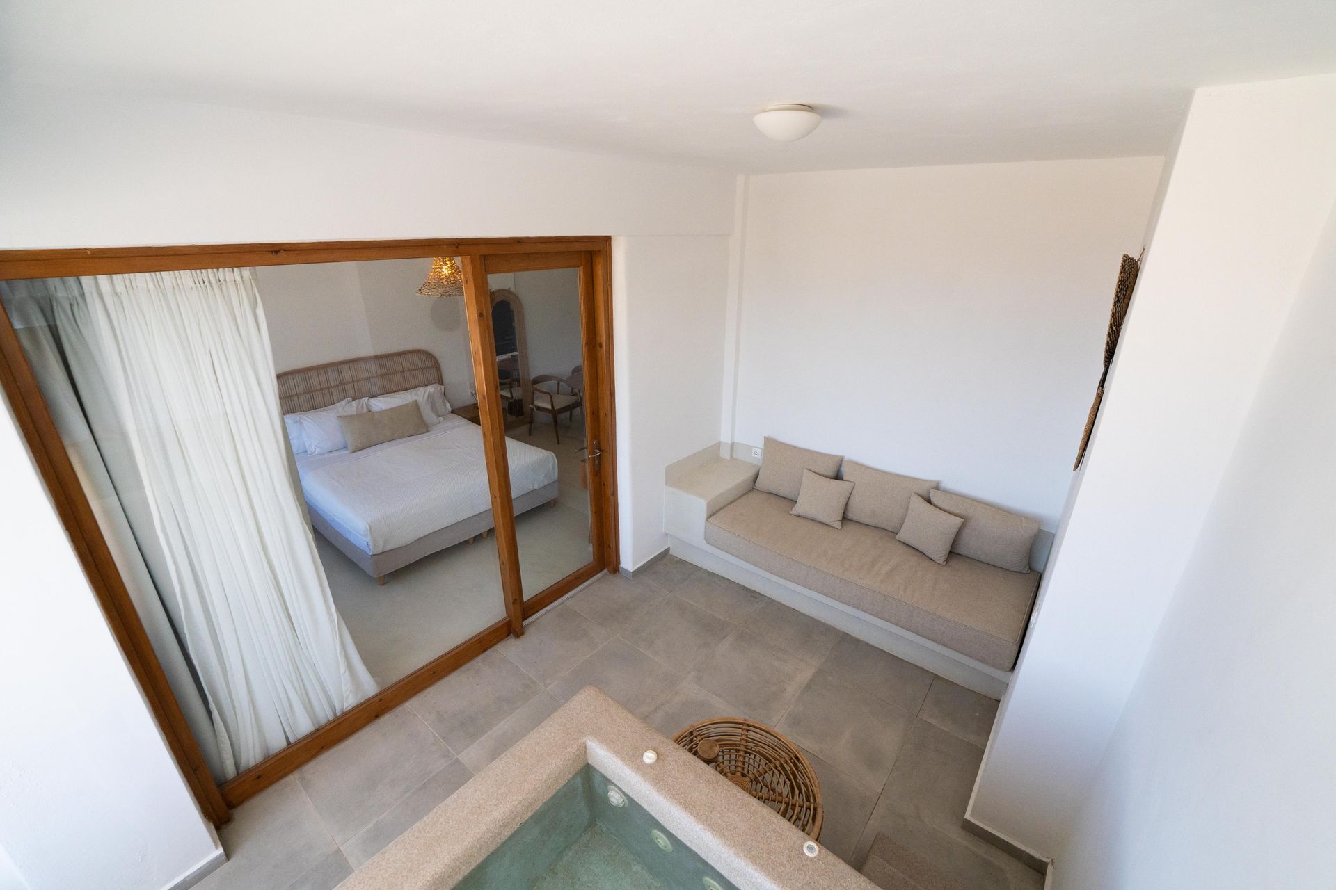 Bedroom with a bed, seating, and a jacuzzi visible through a large sliding glass door.