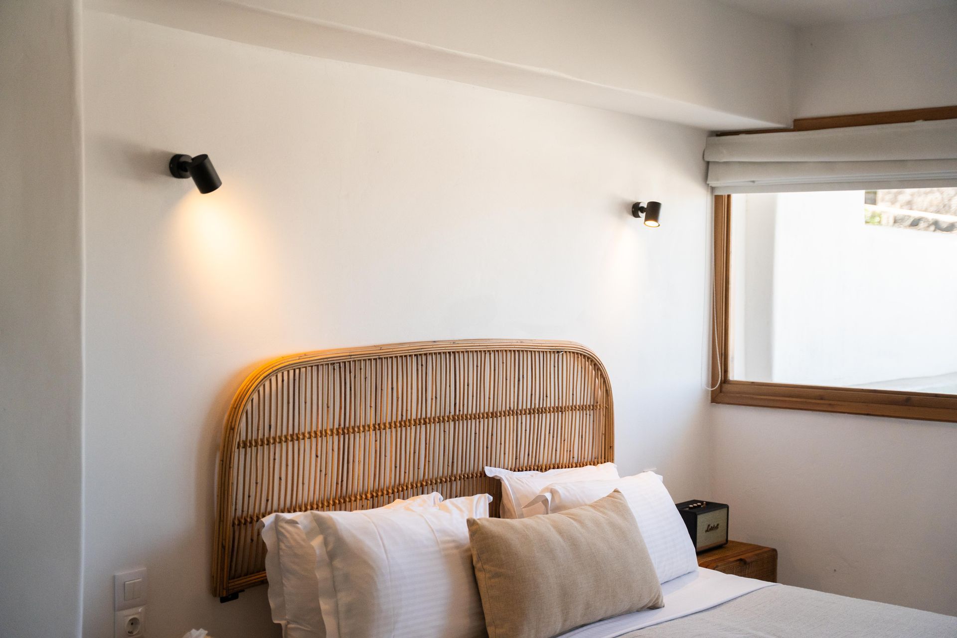 Bedroom with wicker headboard, white linens, bedside table, and two sconces.
