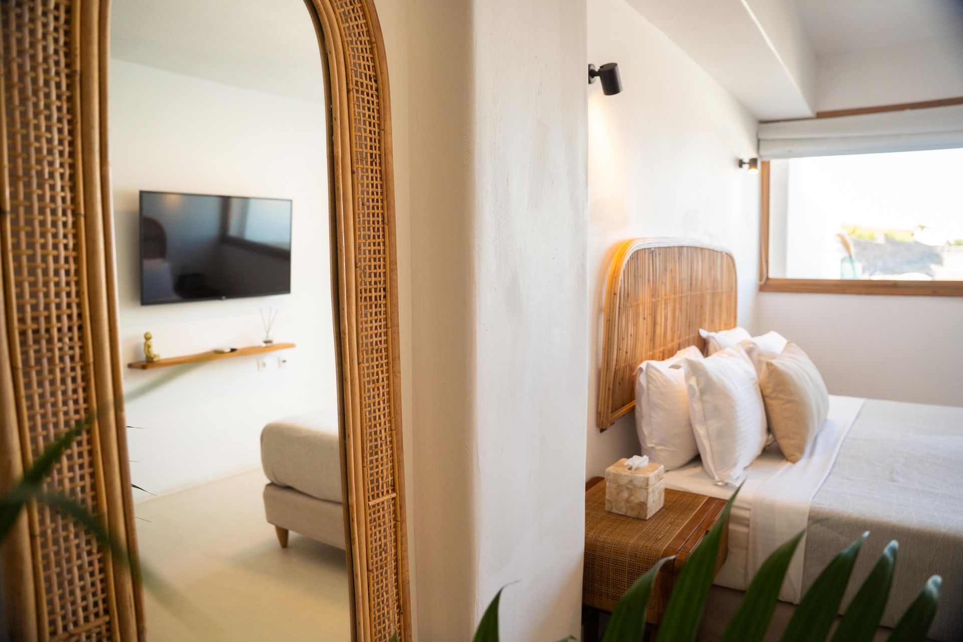 Bedroom with bed and mirror reflecting a living area with a sofa and TV.