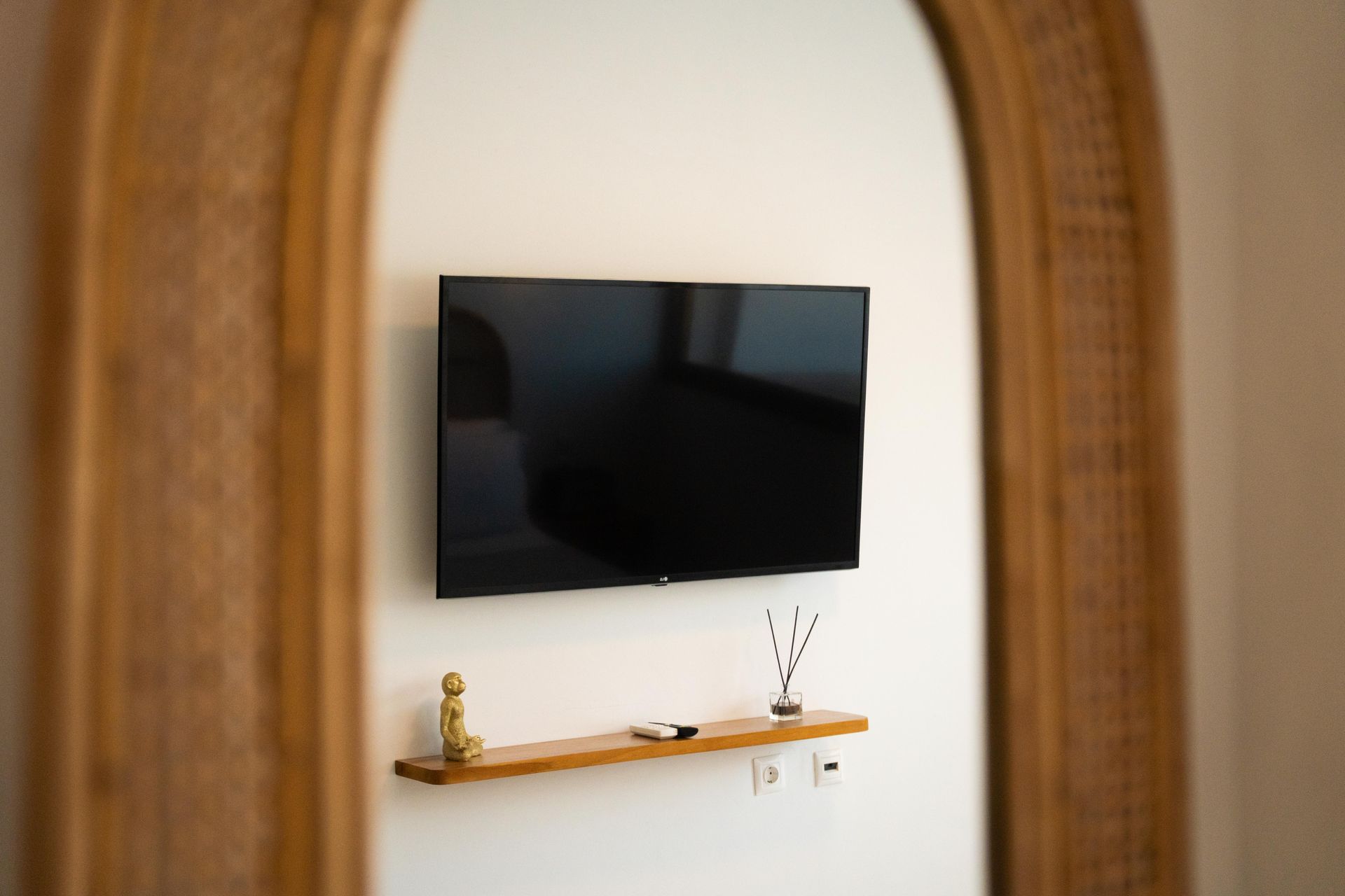 A TV mounted on a white wall with a wooden shelf and decor, framed by a decorative arch.